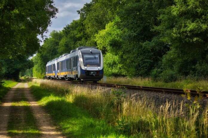 A modern passenger train moving through a scenic, green countryside, emphasizing travel and transportation.