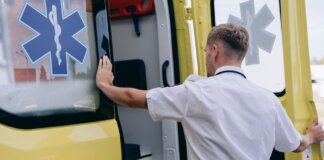 A paramedic in uniform opens the side door of a yellow ambulance during the day.