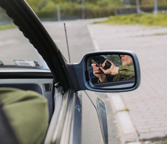 A person with a gun captured in the car's side mirror, suggesting a mysterious scenario.