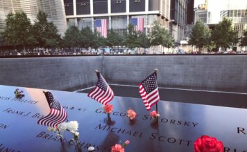 A poignant tribute at the 9/11 Memorial in NYC with flags and flowers honoring victims.