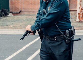 Житель Калгари обвинён в угрозах расстрелом в продуктовом магазине A police officer adjusting a firearm outdoors in a tactical situation, ensuring safety.