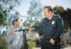 20 лет программе «Молодёжь в полиции» в Дареме A police officer converses with a boy wearing a helmet on a scooter in a sunny outdoor setting.