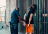 Мужчина обвиняется в сексуальном насилии над двумя детьми A police officer handcuffing a man against a metal fence in an urban area.