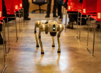 Лидерство Канады в сфере ИИ — в центре внимания конференции ALL IN 2026 A robotic dog navigates an indoor setting amidst red chairs, showcasing technology in modern environments.