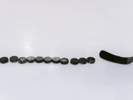 A row of hockey pucks and a stick on an ice rink, perfect for sports content.