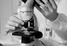 Shared Health продолжает работу лабораторий в расширенном режиме A scientist in a lab coat using a microscope for research in a laboratory setting.