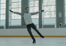 A skilled ice skater executing a graceful move indoors on a rink.