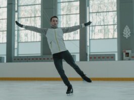 A skilled ice skater executing a graceful move indoors on a rink.