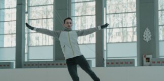 A skilled ice skater executing a graceful move indoors on a rink.