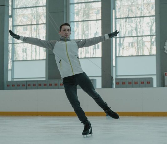 A skilled ice skater executing a graceful move indoors on a rink.