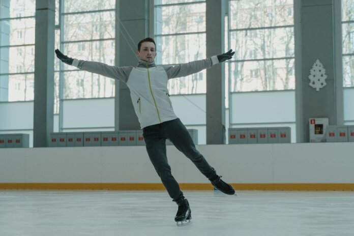 A skilled ice skater executing a graceful move indoors on a rink.