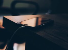 A smartphone connected to a charger lying on a wooden table indoors.