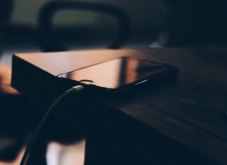 A smartphone connected to a charger lying on a wooden table indoors.