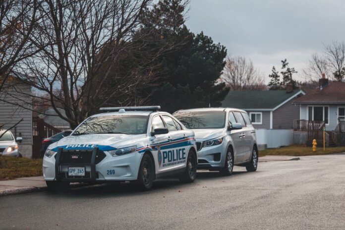 A suburban street with a police car and parked vehicles. Captured in daylight.