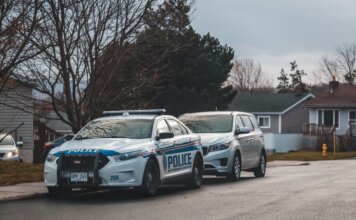 A suburban street with a police car and parked vehicles. Captured in daylight.