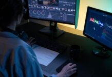 A video editor using dual monitors for editing footage in a dimly lit studio.