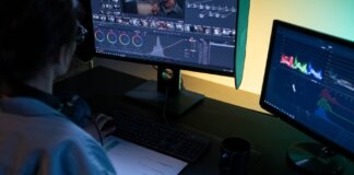 A video editor using dual monitors for editing footage in a dimly lit studio.