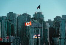 A view of Vancouver's glassy skyscrapers with Canadian and British Columbia flags waving in the foreground.