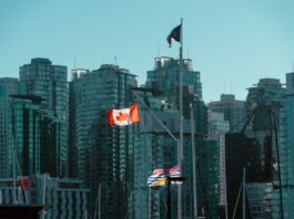 A view of Vancouver's glassy skyscrapers with Canadian and British Columbia flags waving in the foreground.