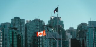 A view of Vancouver's glassy skyscrapers with Canadian and British Columbia flags waving in the foreground.
