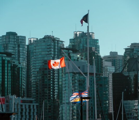 A view of Vancouver's glassy skyscrapers with Canadian and British Columbia flags waving in the foreground.
