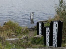 A water level measurement post standing in a lake, surrounded by rocks and vegetation.