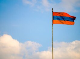Armenian flag on a flagpole swaying in the windy blue sky with clouds.