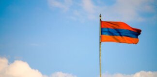 Armenian flag on a flagpole swaying in the windy blue sky with clouds.