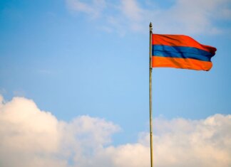 Armenian flag on a flagpole swaying in the windy blue sky with clouds.