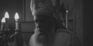 Black and white photo of an Orthodox priest during a candlelit religious ceremony in Cairo, Egypt.