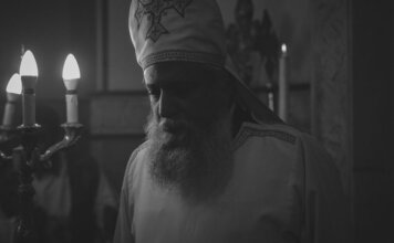 Black and white photo of an Orthodox priest during a candlelit religious ceremony in Cairo, Egypt.