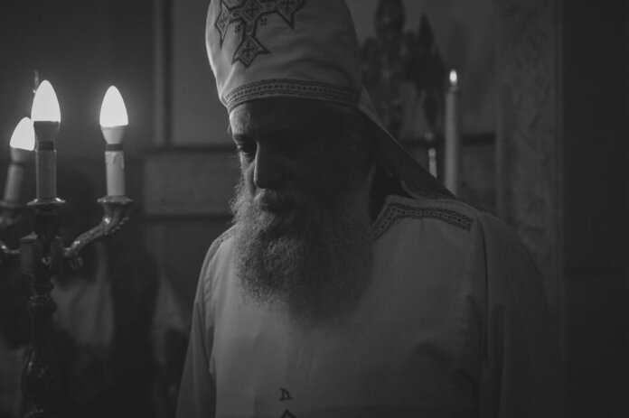 Black and white photo of an Orthodox priest during a candlelit religious ceremony in Cairo, Egypt.