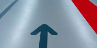Blue arrow and red line on a parking garage floor signify direction and order.