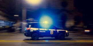 Blurred motion capture of a police car speeding at night with flashing lights on a city street.