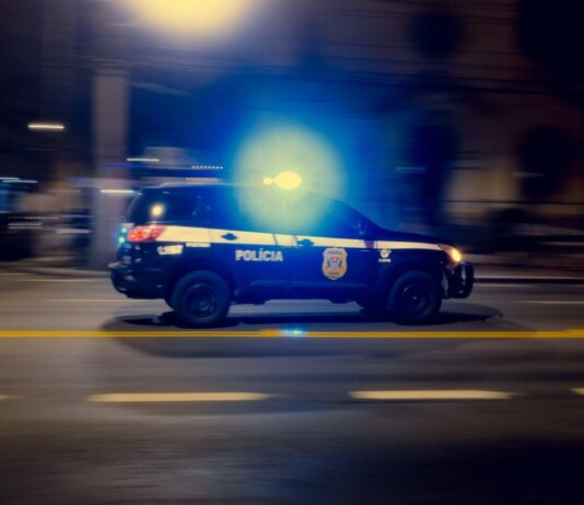 Blurred motion capture of a police car speeding at night with flashing lights on a city street.
