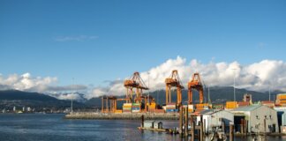 Bright day at a container port with orange cranes and mountain backdrop.