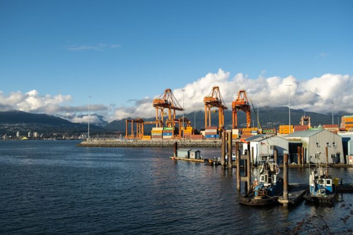 Bright day at a container port with orange cranes and mountain backdrop.