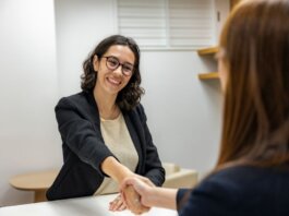 Businesswomen shaking hands in an office, representing a successful job interview or partnership.