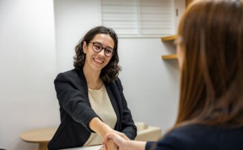 Businesswomen shaking hands in an office, representing a successful job interview or partnership.