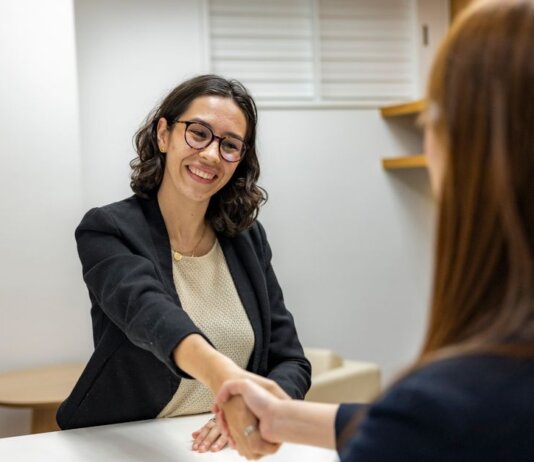Businesswomen shaking hands in an office, representing a successful job interview or partnership.