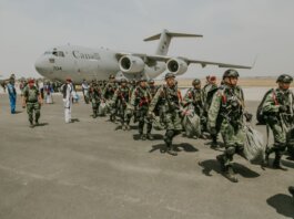 Canadian military paratroopers walk past a C-17 Globemaster on a sunny day at an airport.