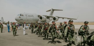 Canadian military paratroopers walk past a C-17 Globemaster on a sunny day at an airport.