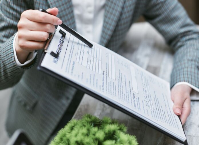 Close-up of a businessperson holding a clipboard with an insurance document, emphasizing details. Close-up of a businessperson holding a clipboard with an insurance document, emphasizing details.