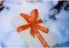 Close-up of a Christmas present with red ribbon nestled in fake snow, creating a festive holiday atmosphere.