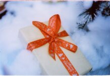 Close-up of a Christmas present with red ribbon nestled in fake snow, creating a festive holiday atmosphere.