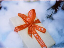 Close-up of a Christmas present with red ribbon nestled in fake snow, creating a festive holiday atmosphere.