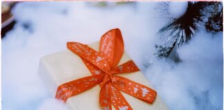 Close-up of a Christmas present with red ribbon nestled in fake snow, creating a festive holiday atmosphere.
