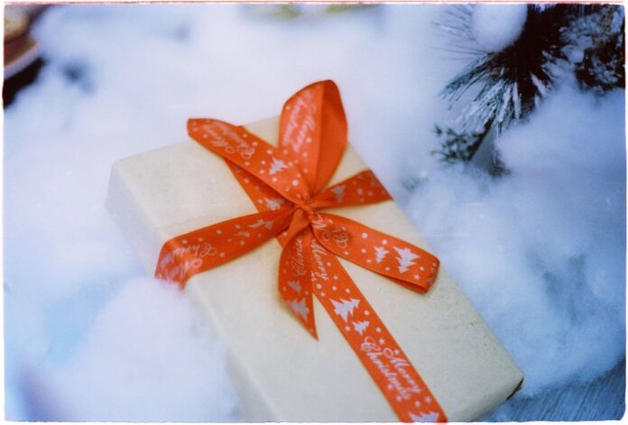 Close-up of a Christmas present with red ribbon nestled in fake snow, creating a festive holiday atmosphere.