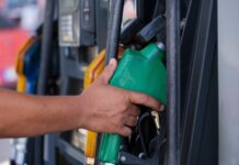 Close-up of a hand holding a green fuel nozzle at a gas pump station outdoors.