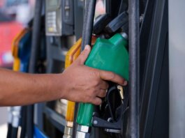 Close-up of a hand holding a green fuel nozzle at a gas pump station outdoors.